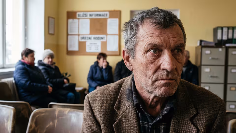 Těsný, trochu mimo střed mužského obličeje, osvětlený ostrým stropním zářivkovým světlem čekárny obecního úřadu.