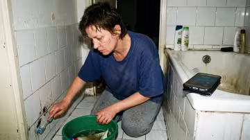 45letá žena klečí na studené dlážděné podlaze s mírně shrbenými zády a metodicky drhne zubním kartáčkem.