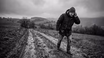 Širokoúhlý záběr při slabém osvětlení zachycený zezadu nebo z boku muže, zdůrazňující jeho osamělý boj s rozlehlou, bezútěšnou krajinou. V popředí dominuje hluboce vyježděná, bahnitá cesta, která vede k postavě muže.